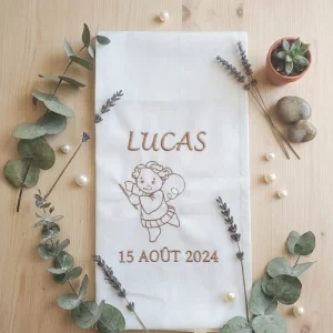 Photo écharpe baptême musicien avec le prénom,la date et un ange musicien.Il y a des feuilles de décoration et Lucas brodé dessus