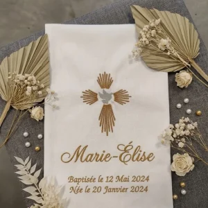Une étole baptême avec une croix moderne et un oiseau au centre .A coté il y a des feuilles d'ornement et quelques décorations