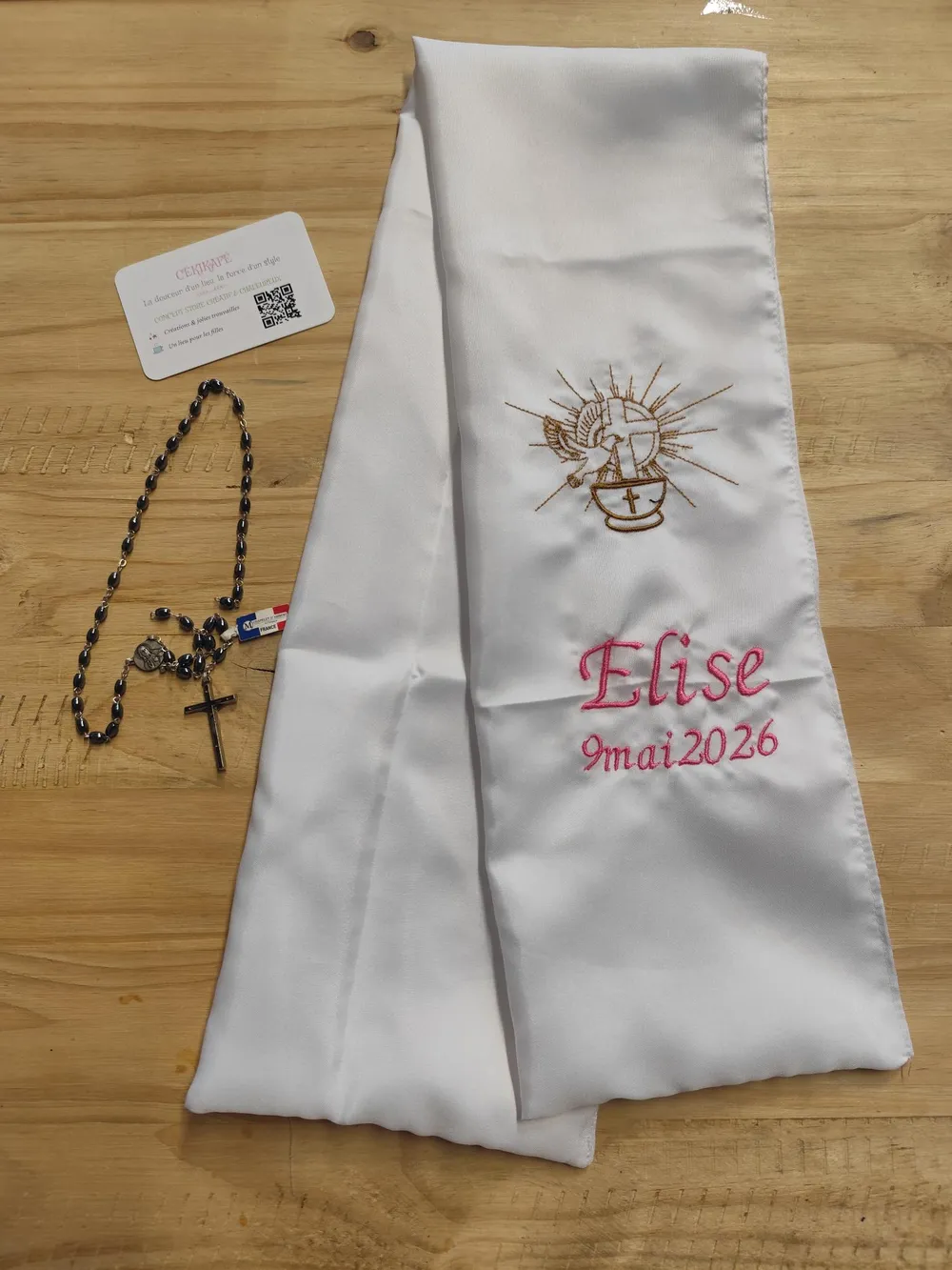 Sur la photo il y a une écharpe de baptême avec une broderie: un calice avec une crois dessus et une autre croix avec colombe.Il y a également le nom de la petite fille et la date de son baptême