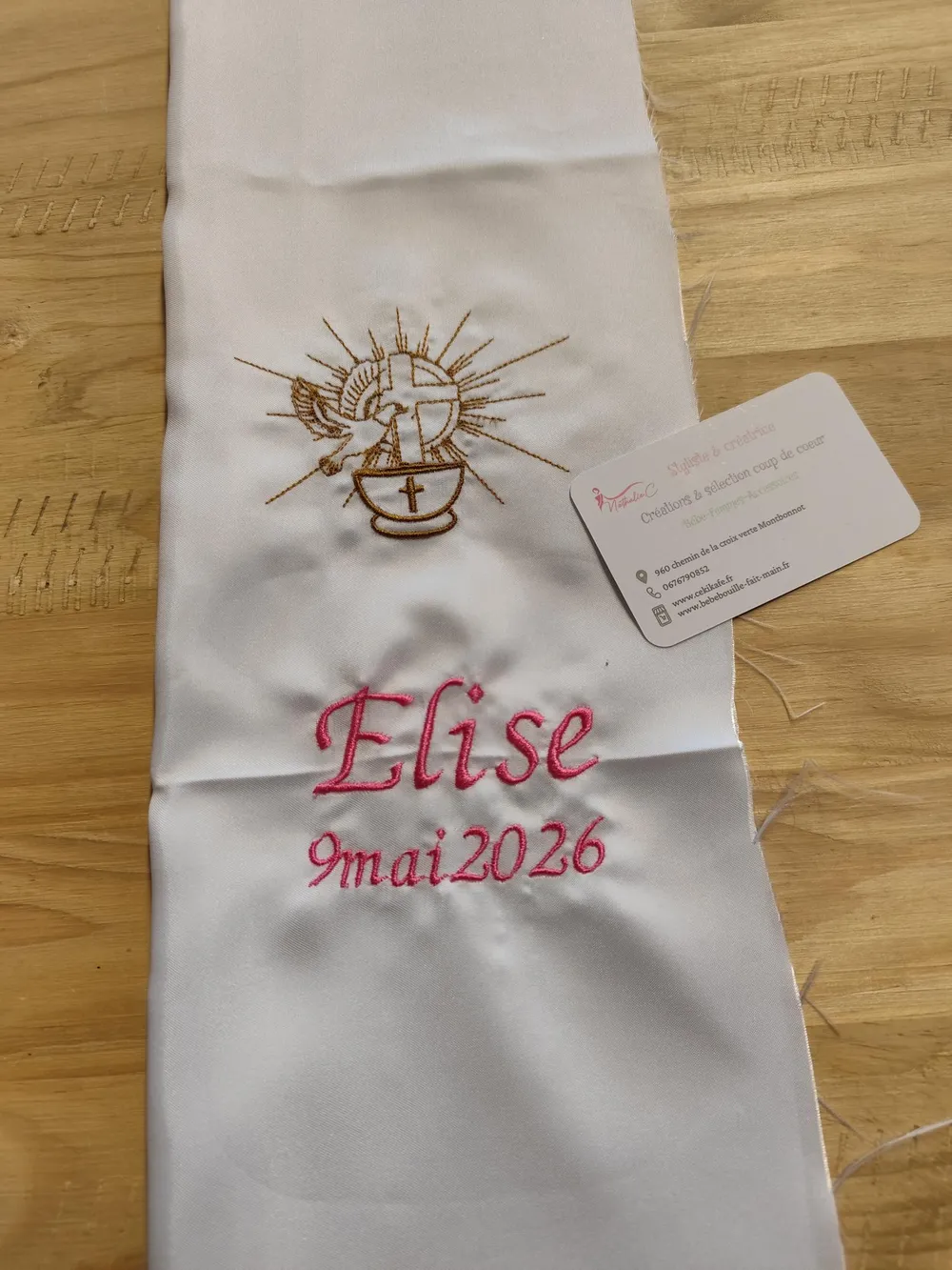 Sur la photo il y a une écharpe de baptême avec une broderie: un calice avec une crois dessus et une autre croix avec colombe.Il y a également le nom de la petite fille et la date de son baptême