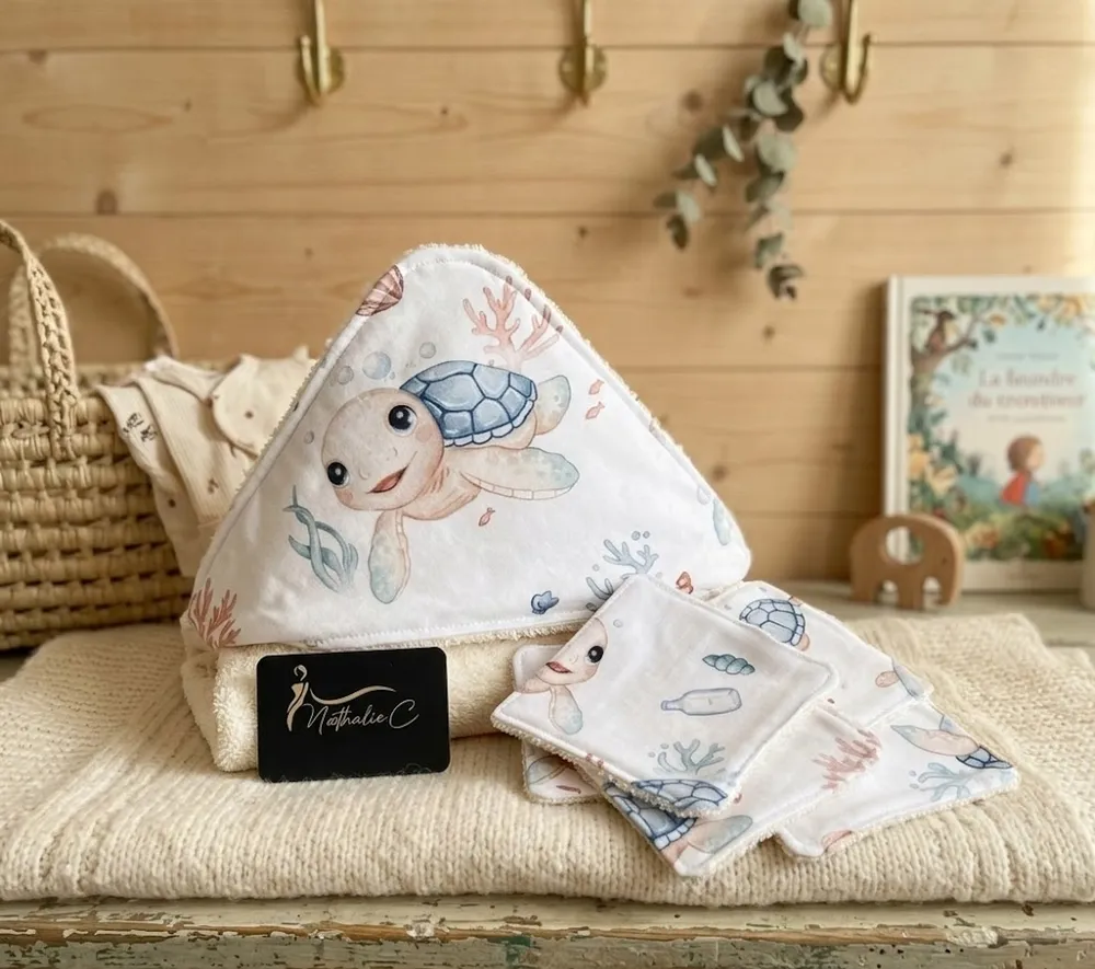 une cape de bain posée sur un meuble, la cape a comme motif des tortues bleues et des lingettes assorties
