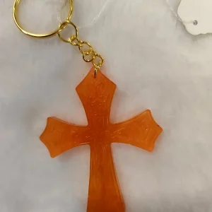 Photo du Porte clé en résine la croix Pierre. Crochet doré et une croix orange .Cette croix est posé sur un tapis blanc