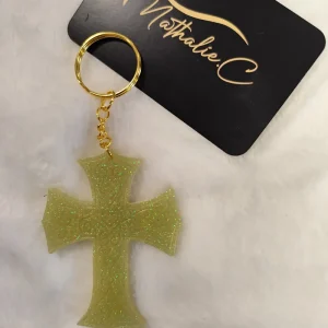 Porte clé en résine ,attache dorée et une croix verte avec du brillant.Cette croix est posé sur un tapis blanc