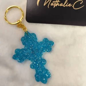 Photo du port clé croix Jean batiste. Le crochet doré et une croix bleue avec des brillant.Cette croix est posé sur un tapis blanc
