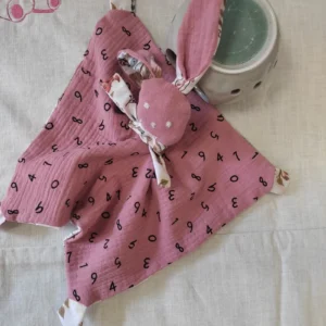 un doudou en gaze de coton rose avec des lettres dessus.le visage est brodé à la main et ce doudou lapin est fait dans une carré.