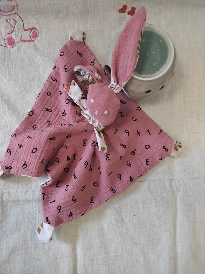 un doudou en gaze de coton rose avec des lettres dessus.le visage est brodé à la main et ce doudou lapin est fait dans une carré.