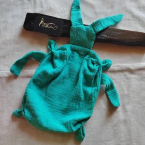 sur l'image il y a un doudou en gaze de coton vert posé sur un drap blanc
